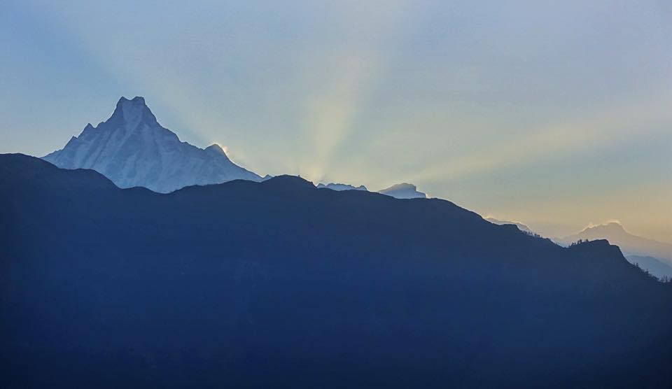 Rays of sun shine from behind a mountain with a fish-tail shaped peak at sunrise