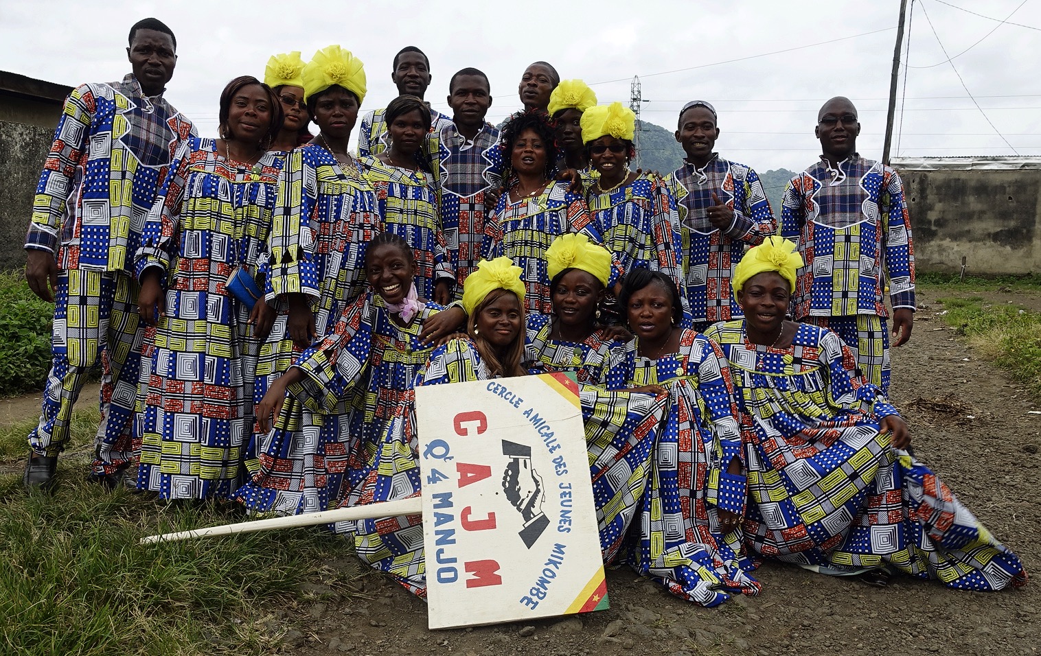 A group of people all wearing clothes made from the same cloth pose with a sign for their group