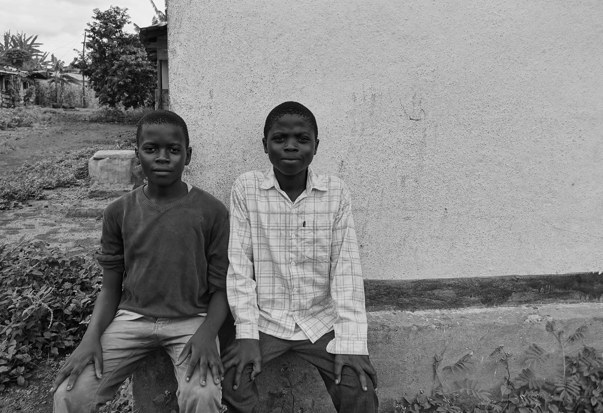 Two boys sit on a ledge in front of a white wall looking at the camera