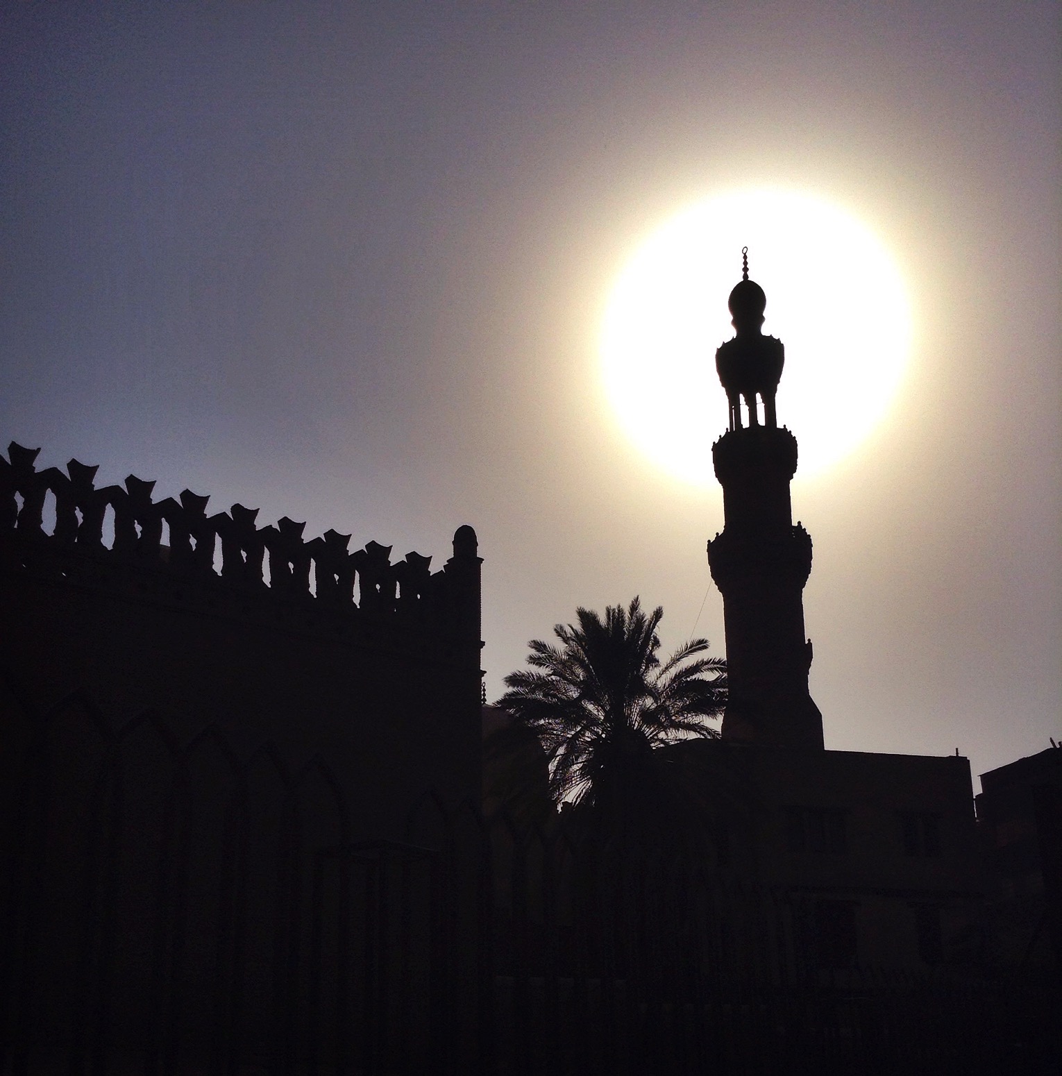 A minaret of a mosque silhouetted with the sun directly behind it