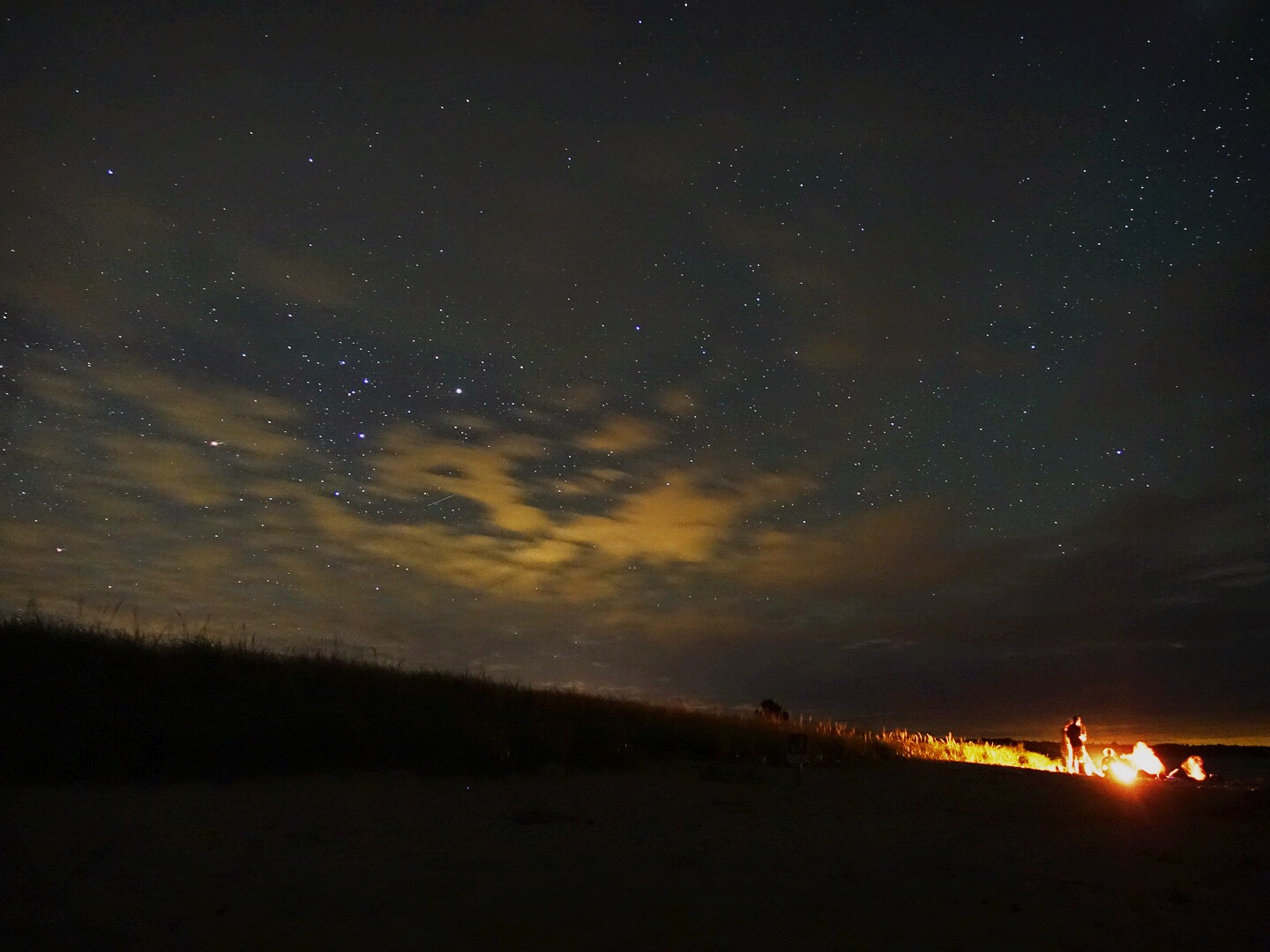 A campfire on the right side under a night sky with low yellow clouds