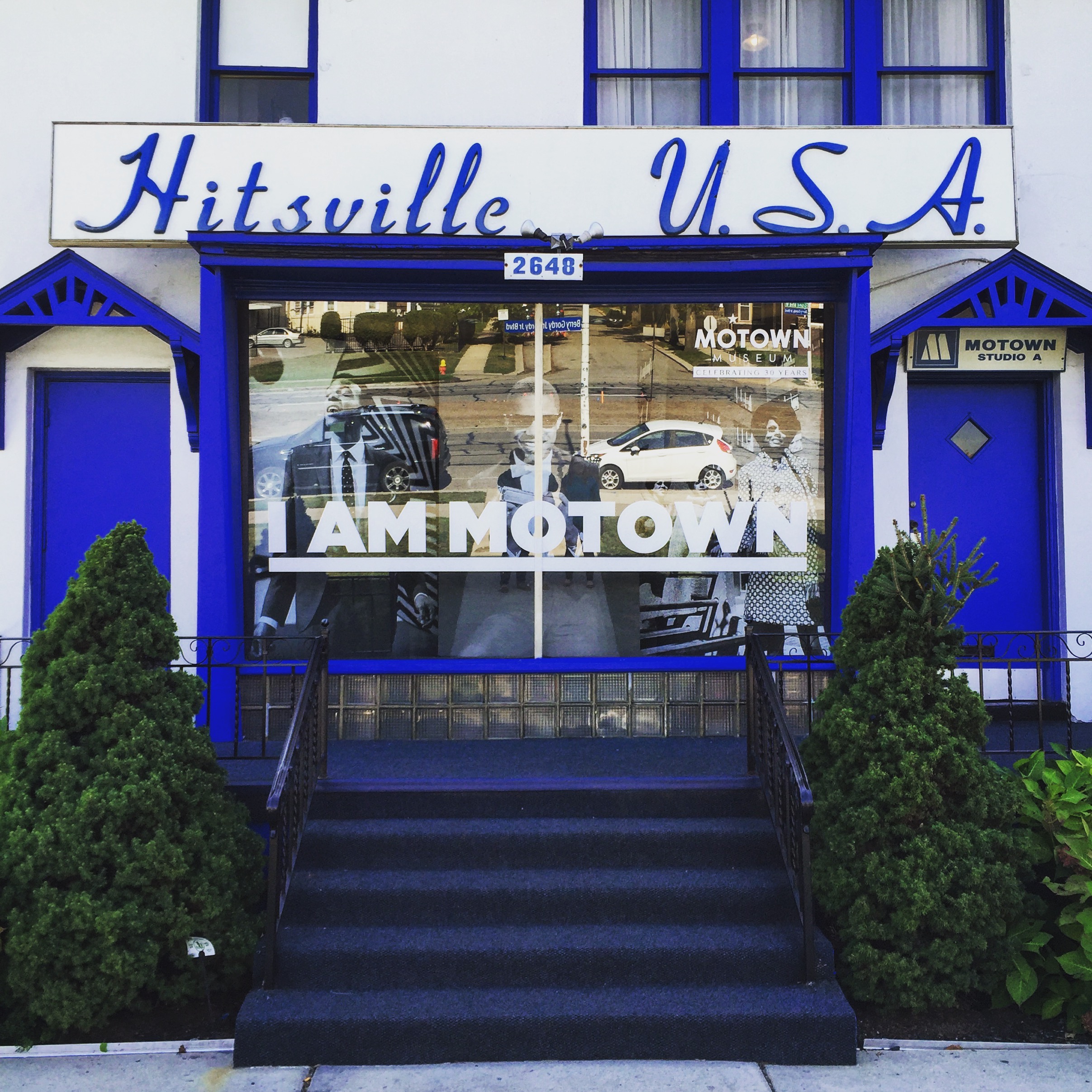 The front of a white house with blue doors and trim and the words Hitsville, USA on a sign