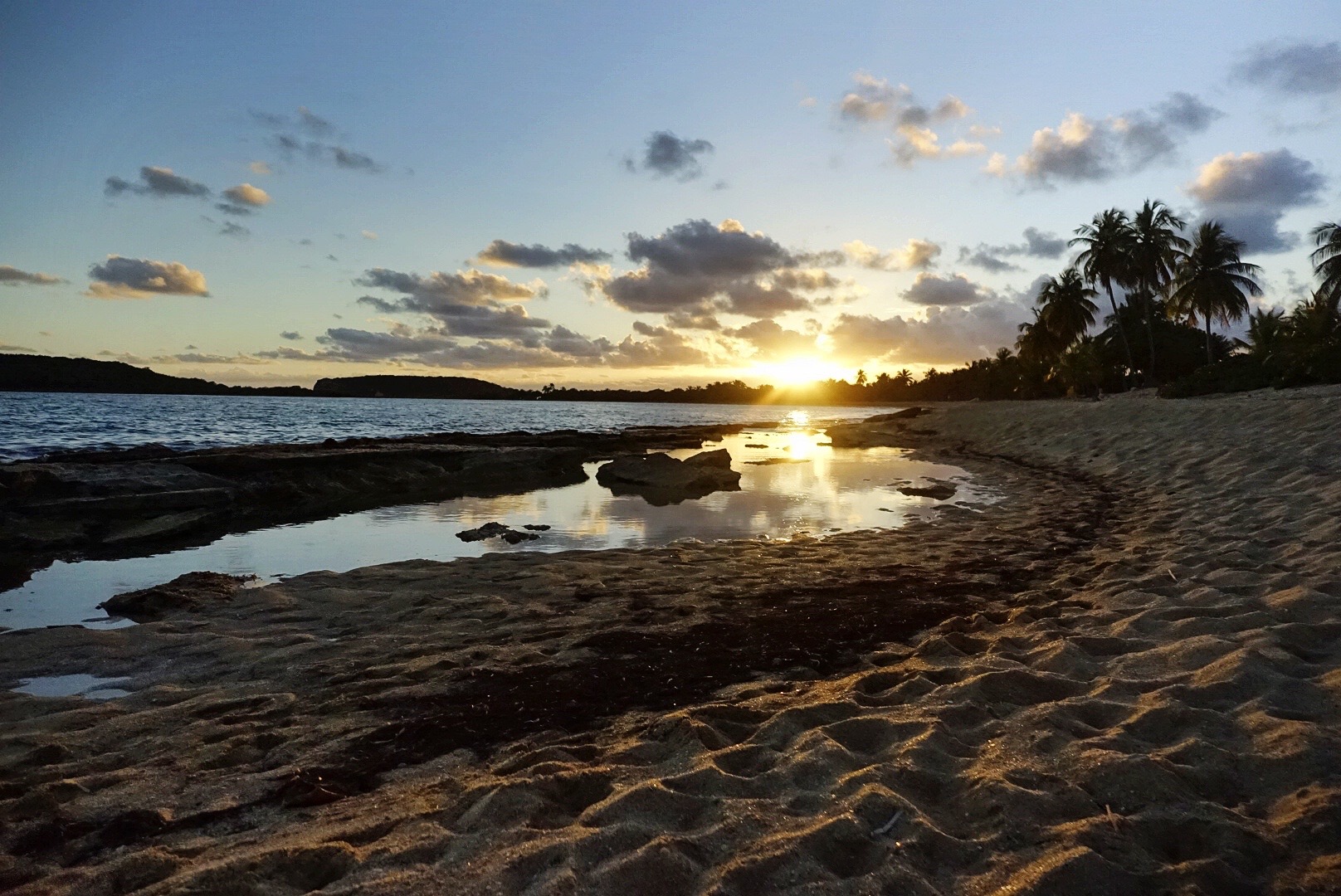 the sun set over the ocean with tide pools in the foreground