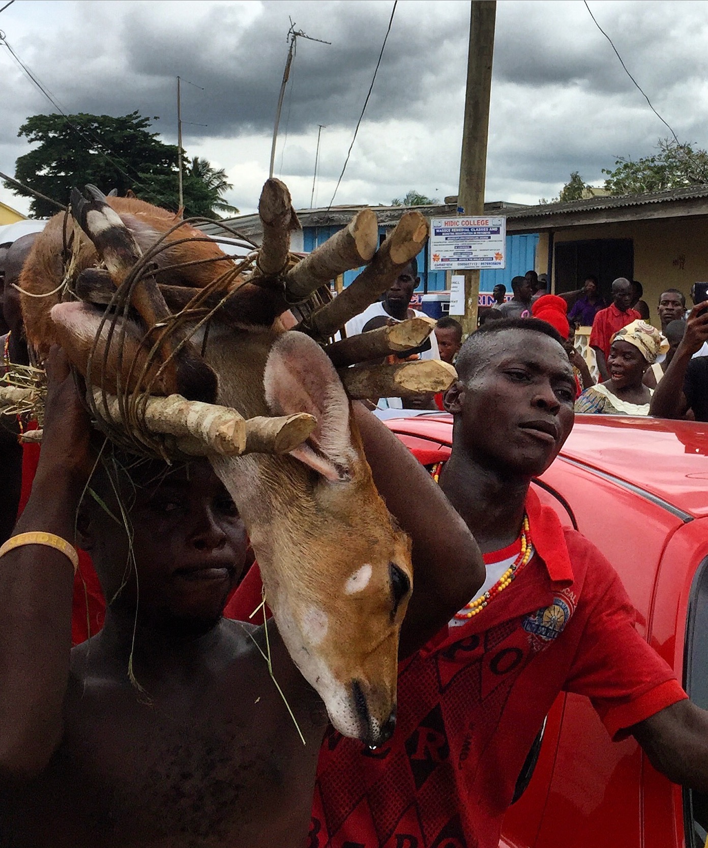 a man carrying a tied up deer on his head with another man escorting him through the streets