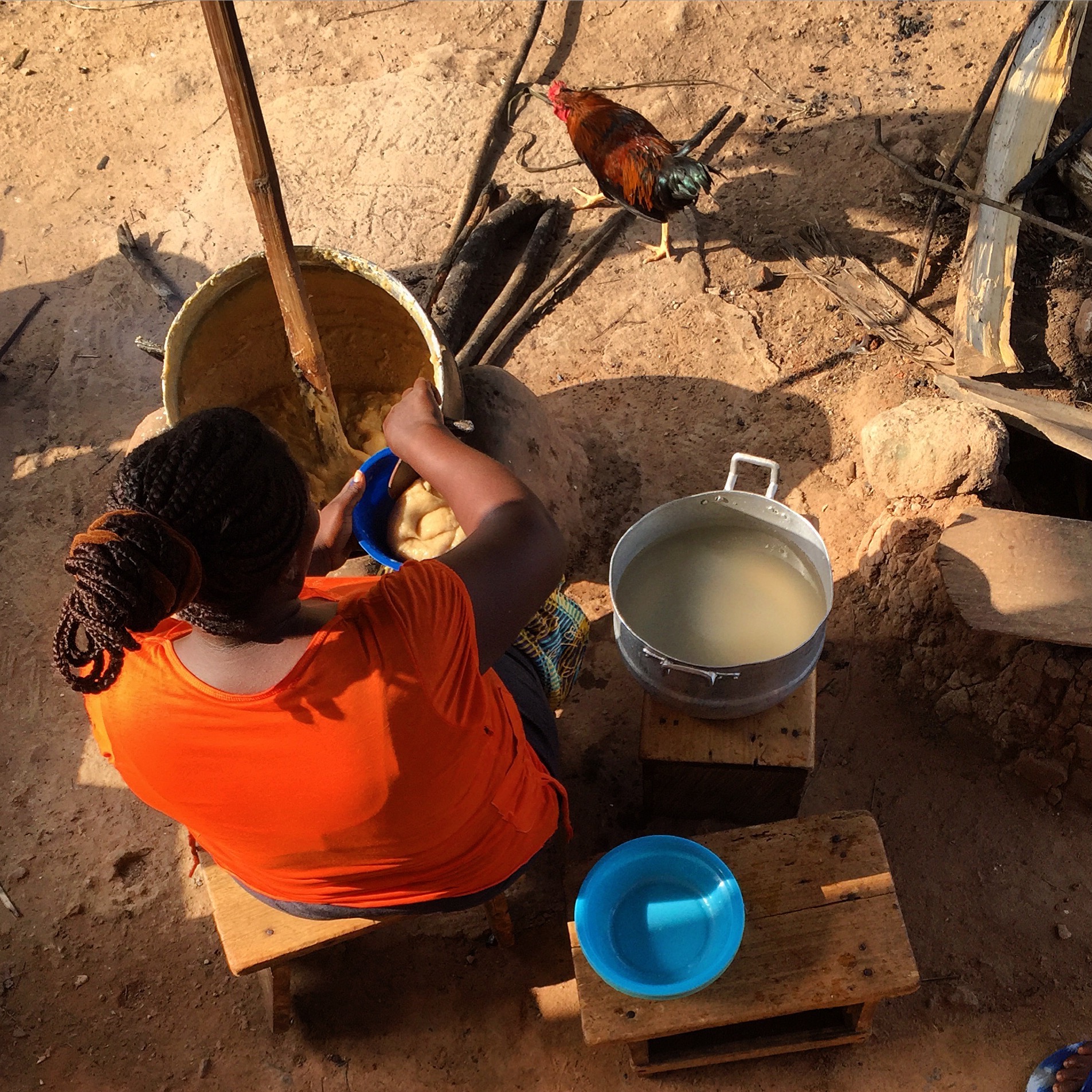 a view from above a seated woman with large pots around her as she makes konkonte