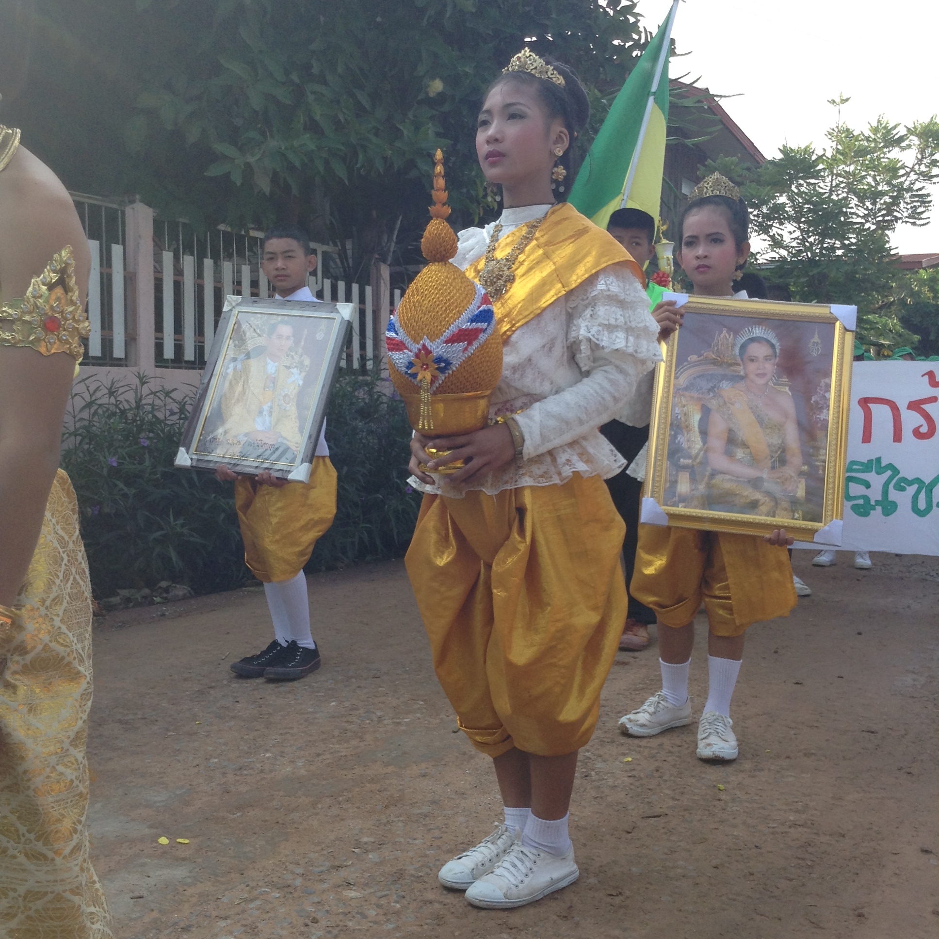 young thai children wearing traditional clothing carrying pictures of the thai king and queen