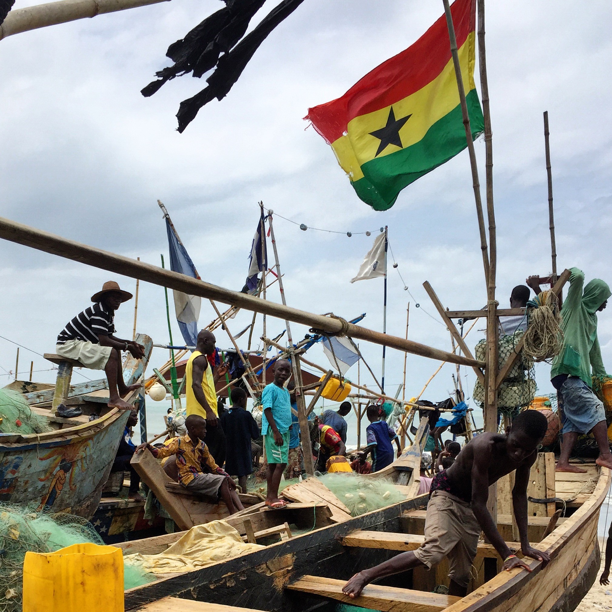 a few people standing on beached wooden fishing boats with flags flying above