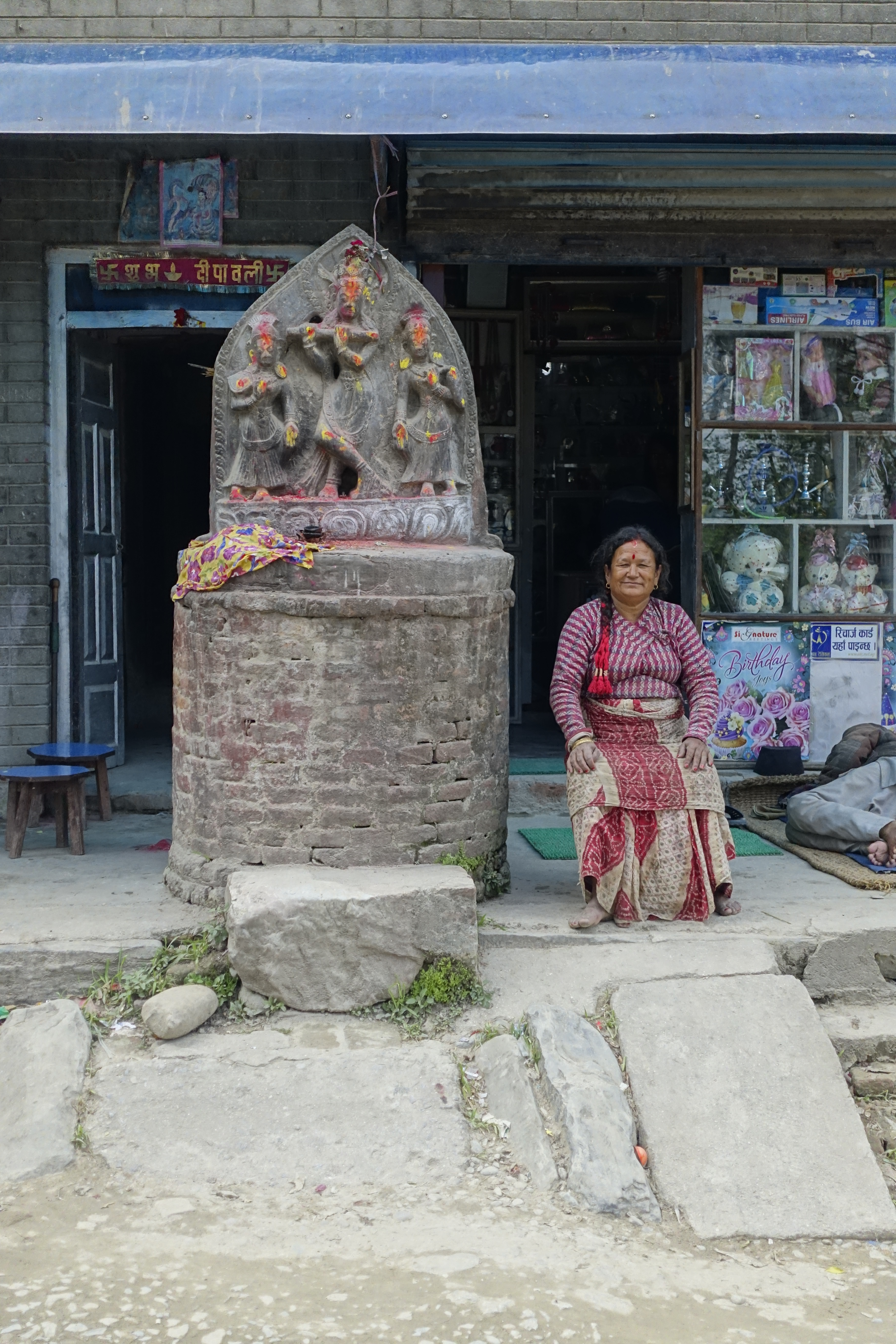 hindu deities carved in a rock in front of a shop with a woman sitting next to it