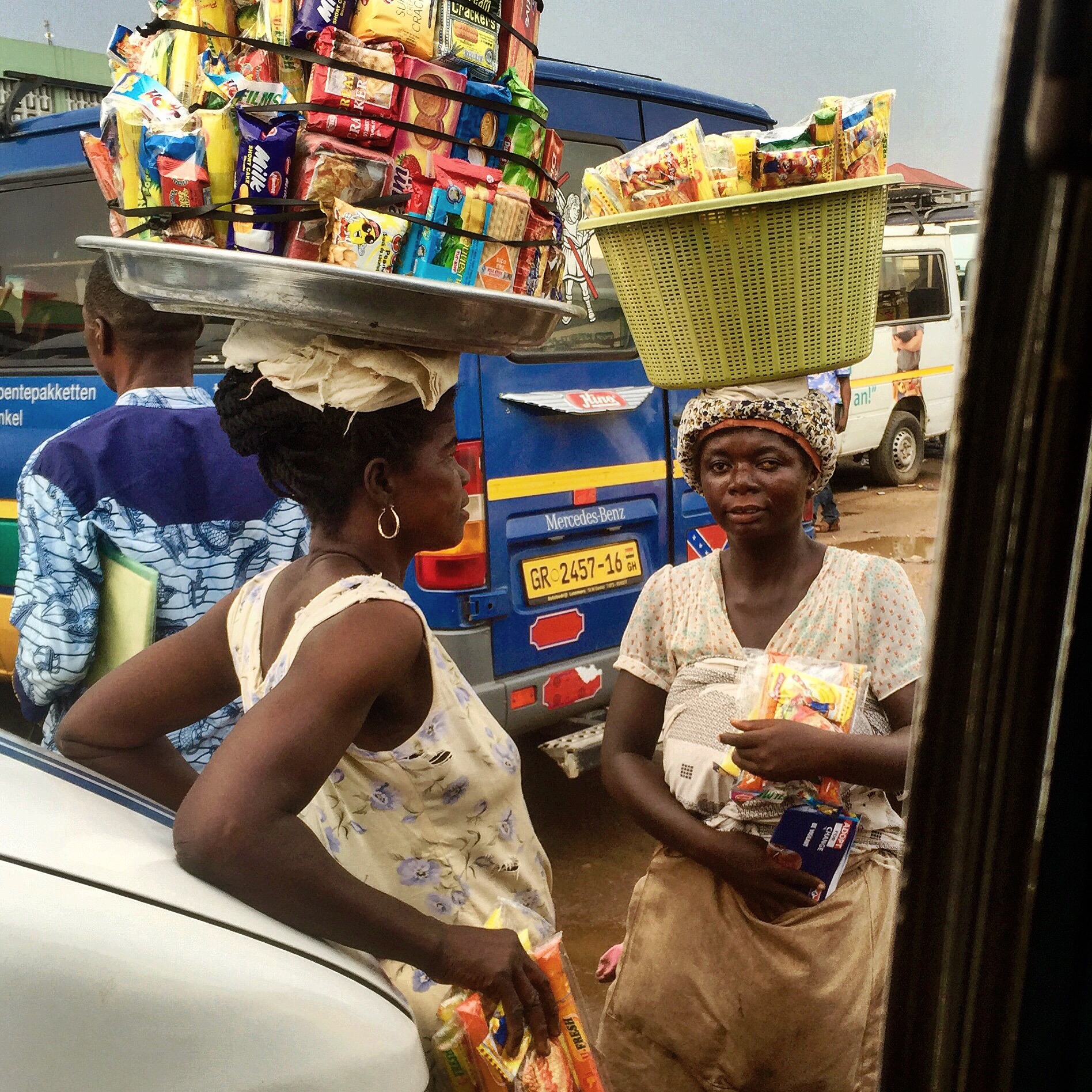 Two women talking with baskets on their heads filled with packets of crackers and cookies