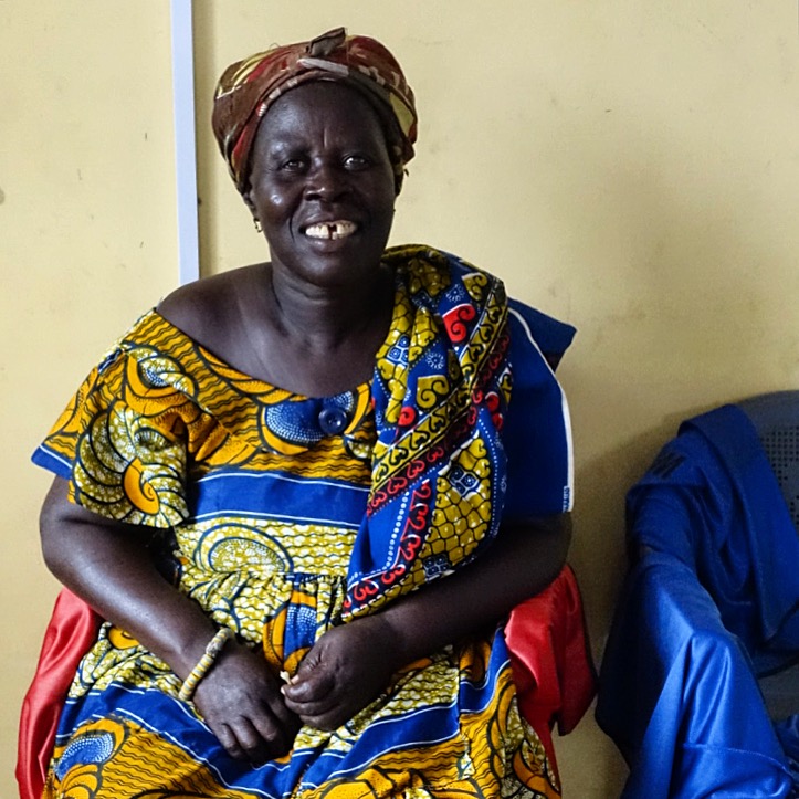 A woman wearing an African print dress is looking at the viewer and smiling.