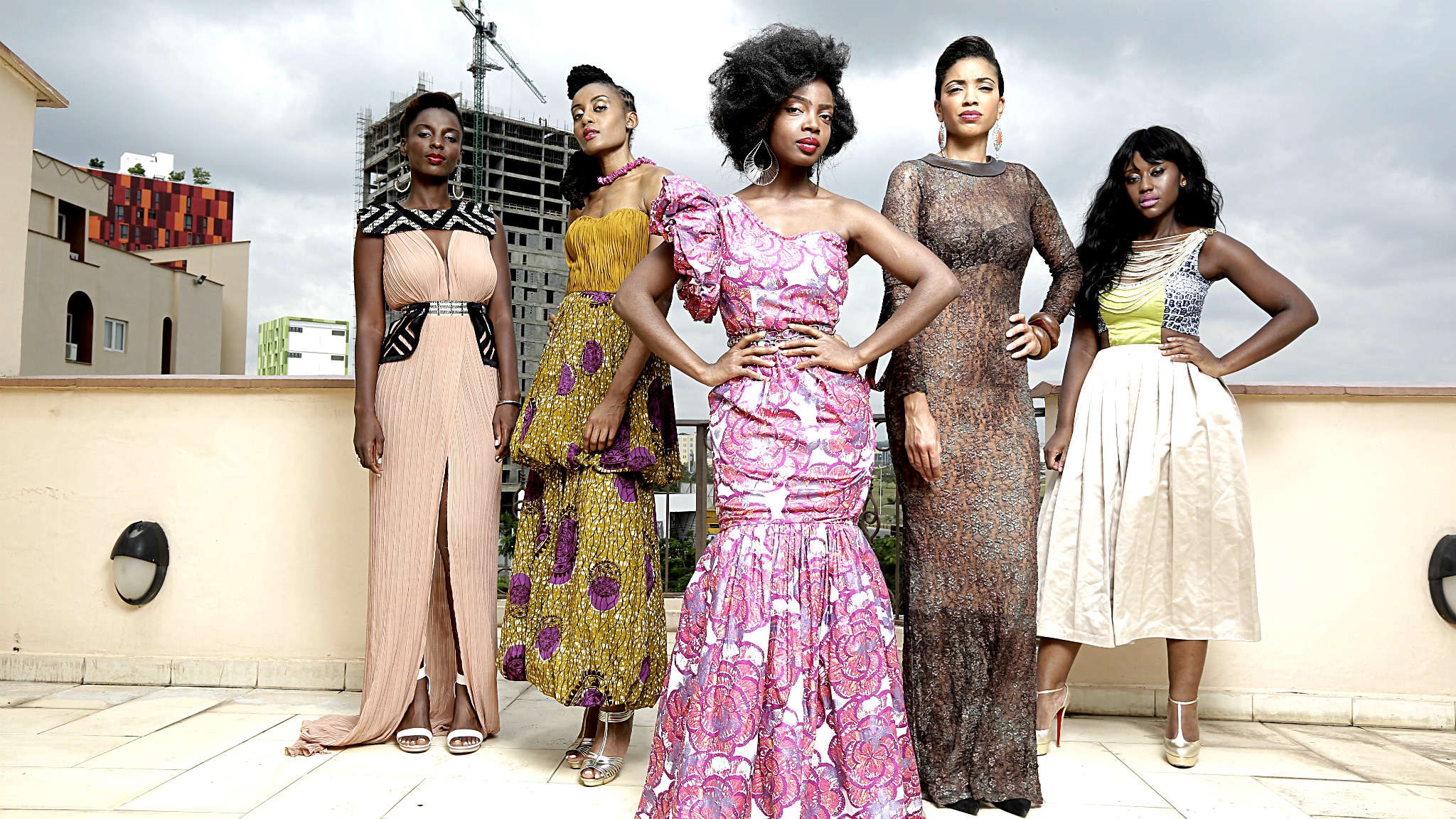 Five women wearing stylish dresses stand on a rooftop.