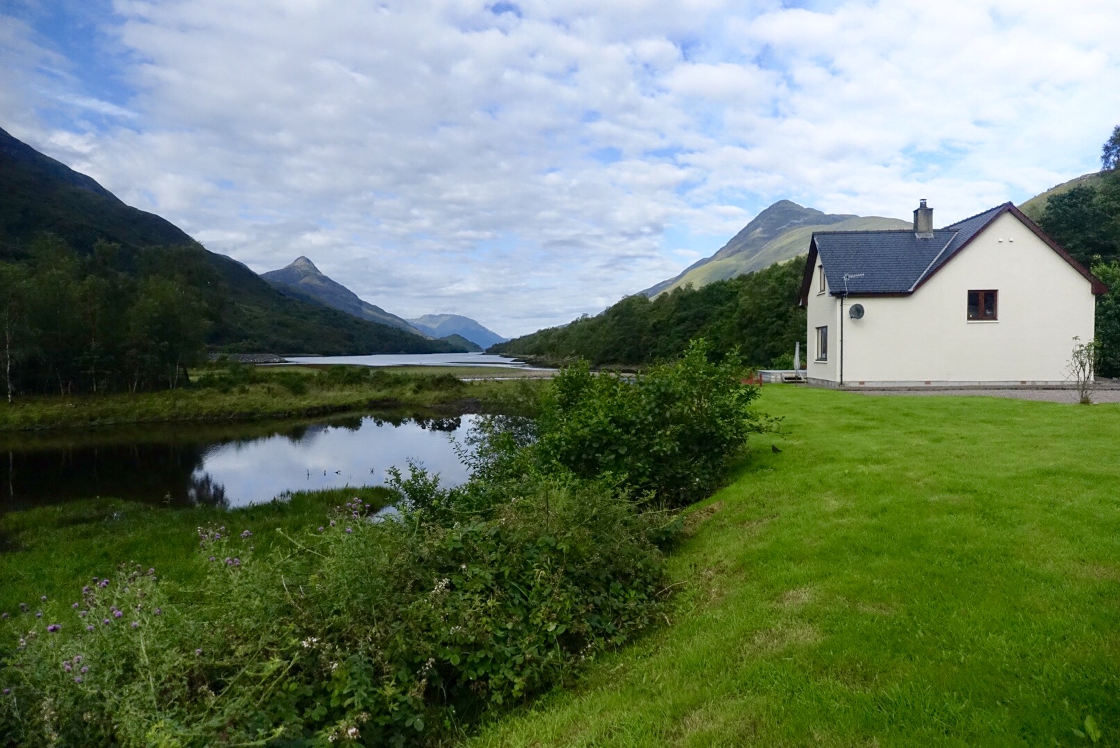 View of a lake surrounded by mountains with a white house on the right. on the West Highland Way